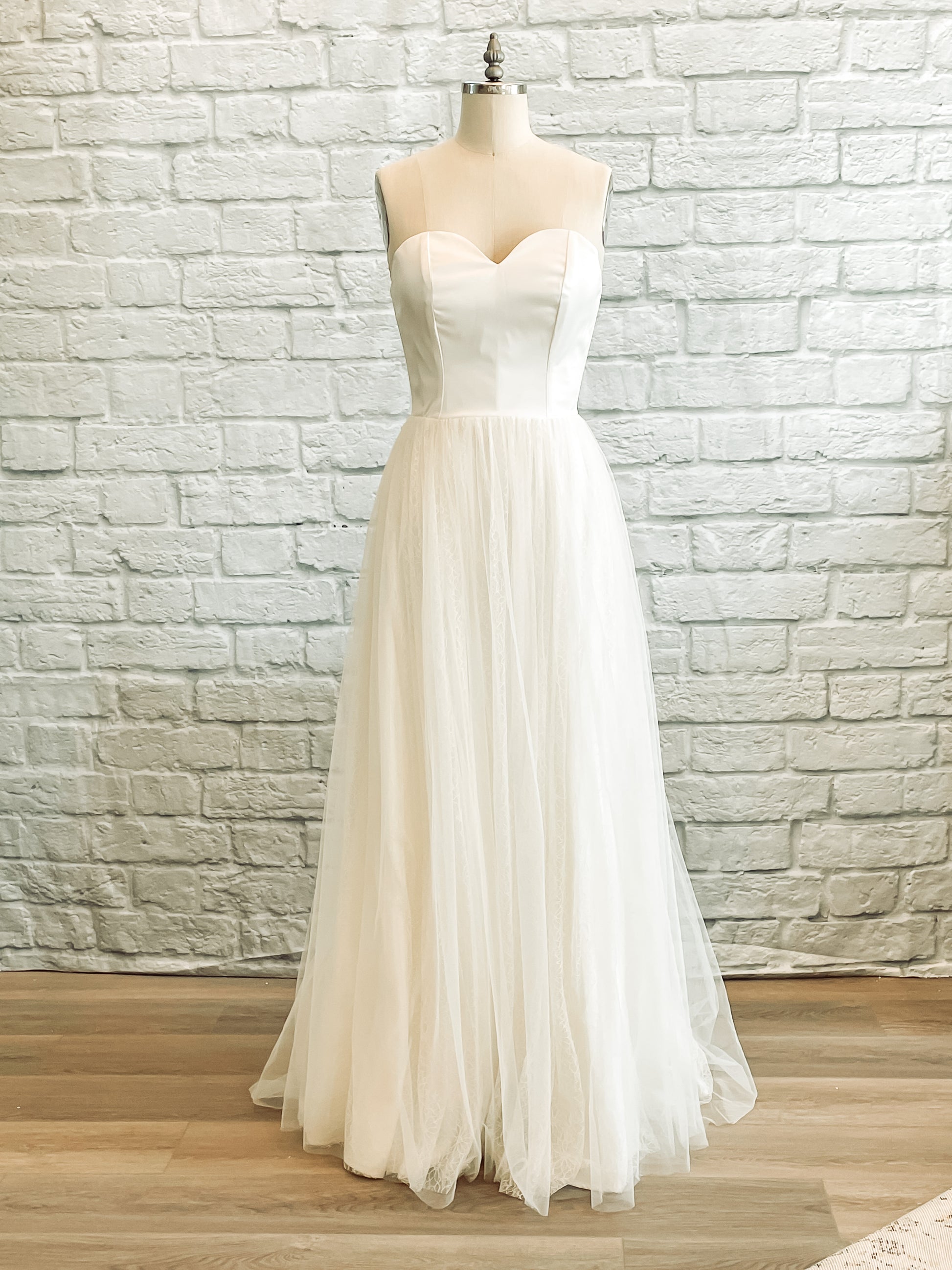 A-line wedding gown with a sweetheart neckline, shown on a mannequin. The Beatrice gown features layered tulle and daisy lace over a satin base for a soft, romantic silhouette.