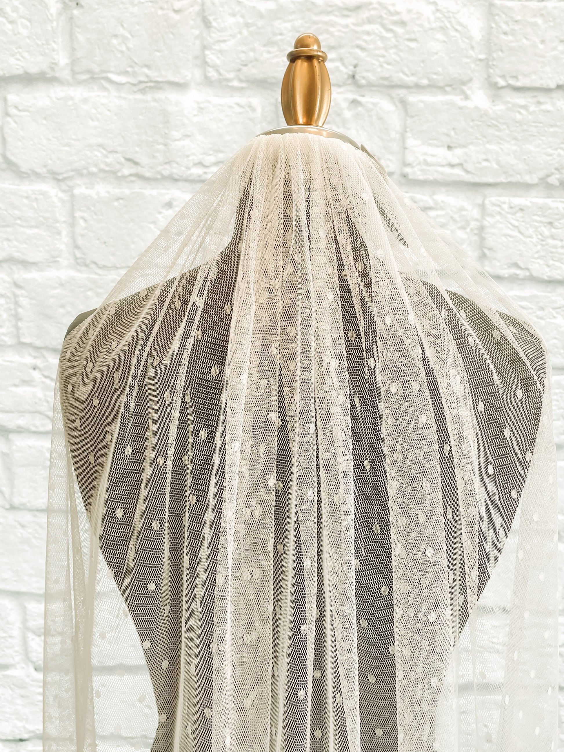 A close up of the gathered comb and top pf the swiss dot veil, scarlett. displayed on a dark mannequin you an easily see the  ¼" dots on tulle veil. 