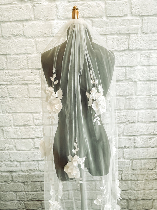A close up image of the Celine wedding veil with 3D satin and organza flowers in a calf length displayed on a mannequin. the image is cropped so we only see the top 2/3rds of the veil.