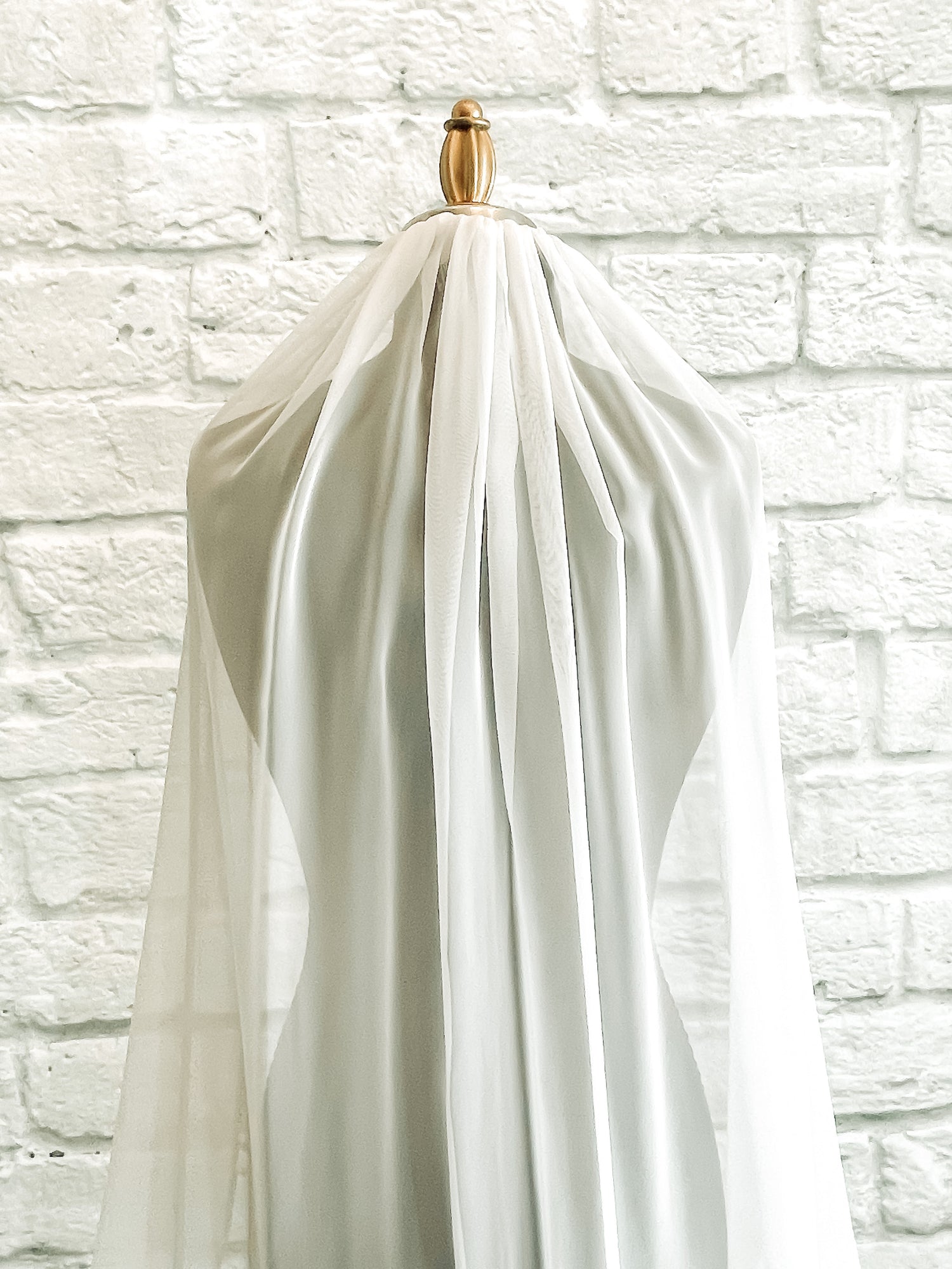 A close up of the Braelyn, chiffon veil, displayed on a mannequin; she has gatheres at the top of the omb and falls down in gentle folds. 