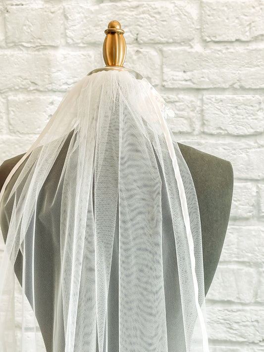 Vintage-inspired nylon tulle wedding veil with satin trim on a mannequin.