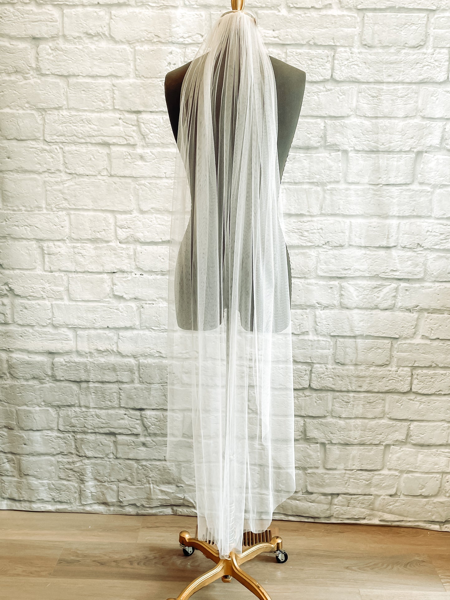 A full length photo of the Jane veil on a mannequin. It is shown in white and a waltz / calf length. The gathering at the comb creates many folds in the tulle as it falls. 