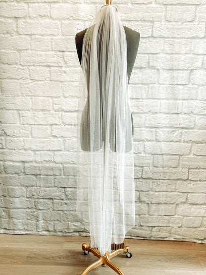 A full length photo of the Jane veil on a mannequin. It is shown in white and a waltz / calf length. The gathering at the comb creates many folds in the tulle as it falls. 