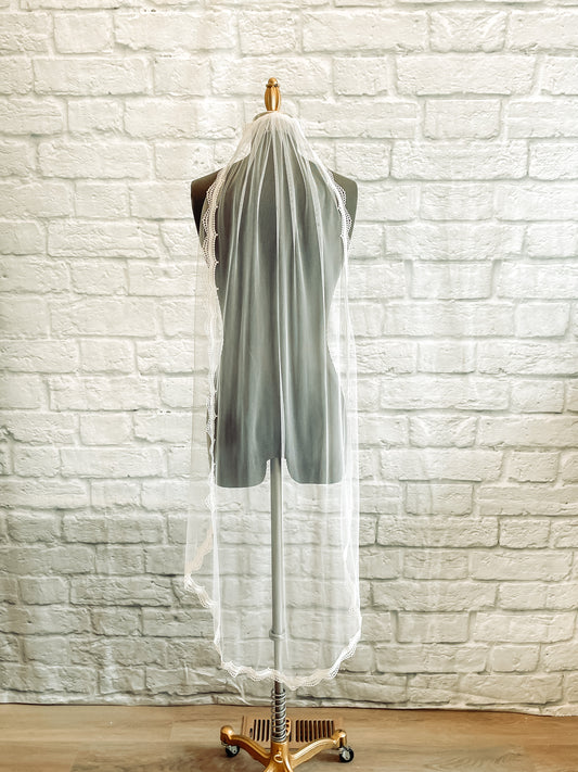 A full length photo of the scalloped edge embroidered lace wedding veil on a mannequin shown here in a waltz length– Brennan veil. 
