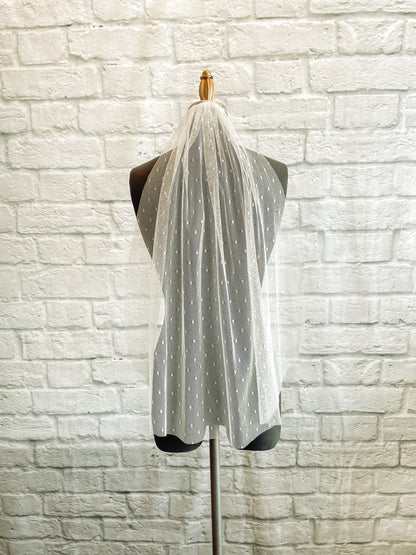 Another Scarlett dot veil made from a swiss dot tulle and comb; it is being shown against a dark grey mannequin and is shown in this image in a Fingertip length.