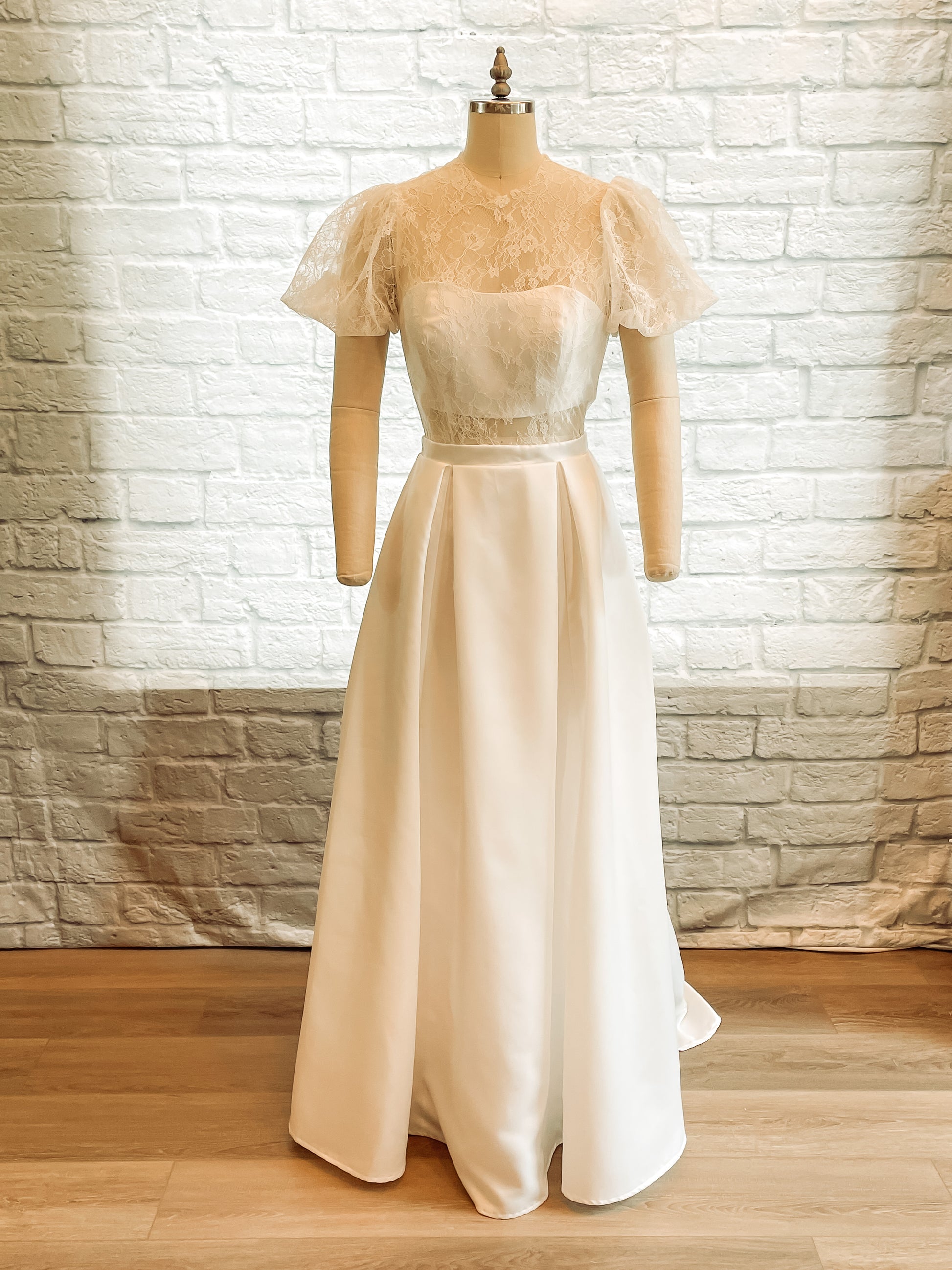 Jessa bridal gown on a mannequin with sheer lace bodice, high neckline, and pleated satin skirt.
