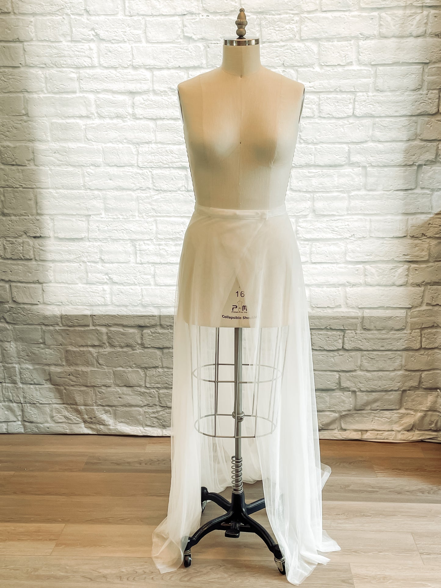 A full front of the Pale ivory wrap-style soft tulle overskirt, deon, shown on a mannequin. 