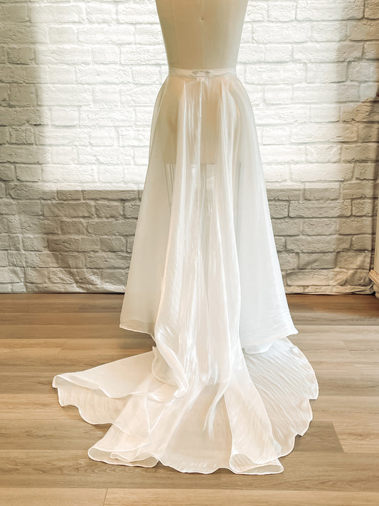 Back view of Amber overskirt showing high-low cut and dramatic ruffle details extending into a 25-inch train
