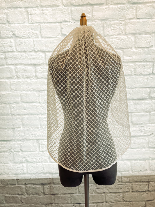A full length shot of the Gloria bridal veil in a fingertip length. The veil has been displayed on a mannequin and is pulled over the mannequins shoulders. to show the full width of the veil with a pale ivory ribbon edge and clear sequins.