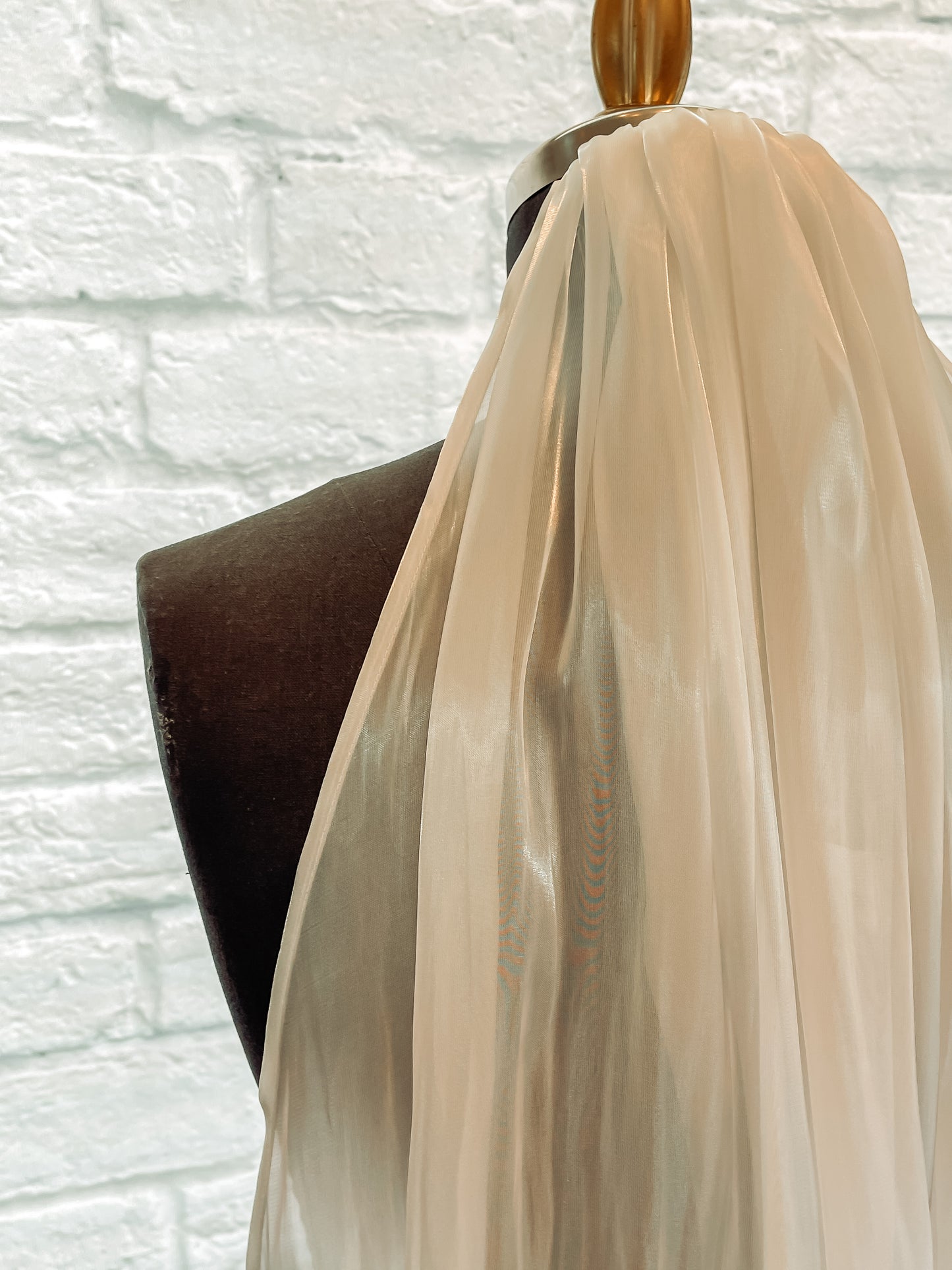 A Close-up of luminous organza bridal veil pinned to a Mannequin. The finished edge is shown off against the dark mannequin. 