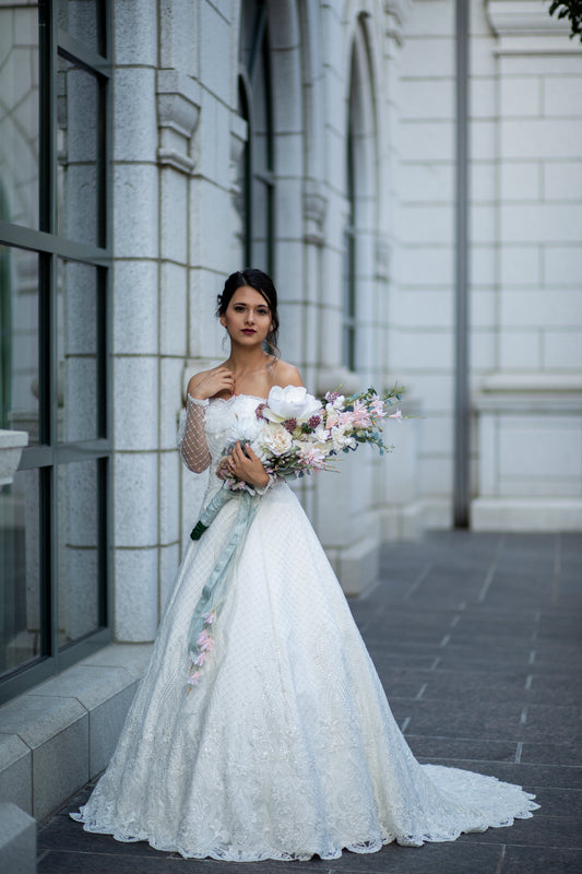 A full length shot of a bride wearing the Virginia gown; the gowns lace, diamond tulle, and stunning train are all a feature. 