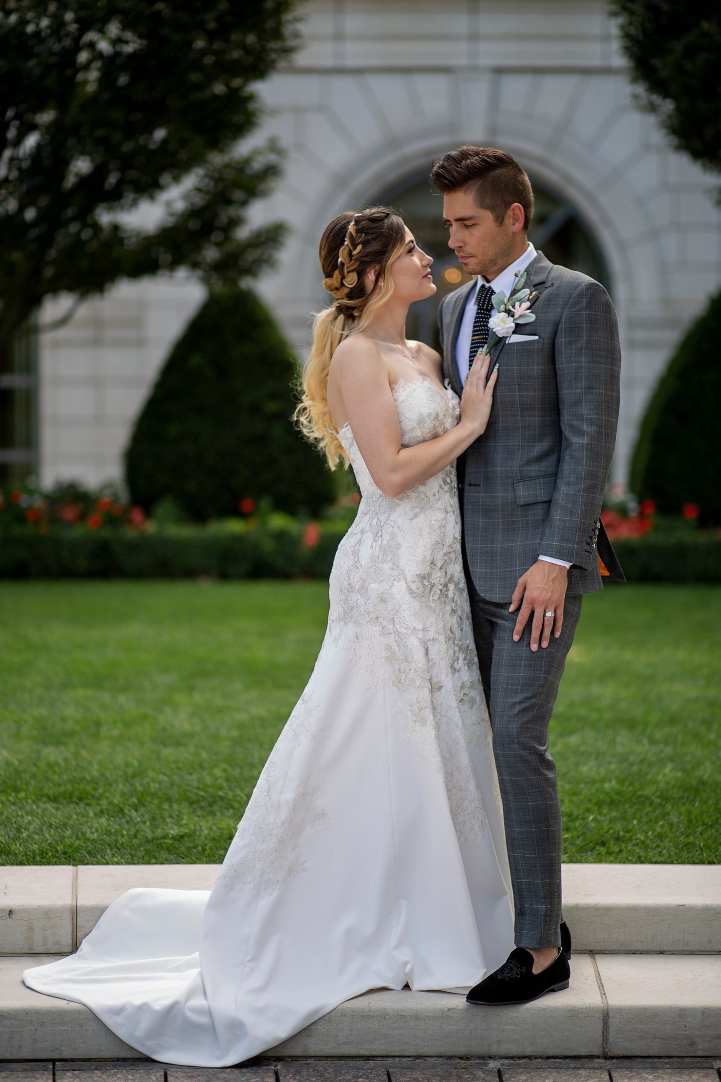 Bride standing with her groom; showing the Side profile of the giselle gown. The curve-hugging bodice and gradient lace detail leads into the 18" train. 