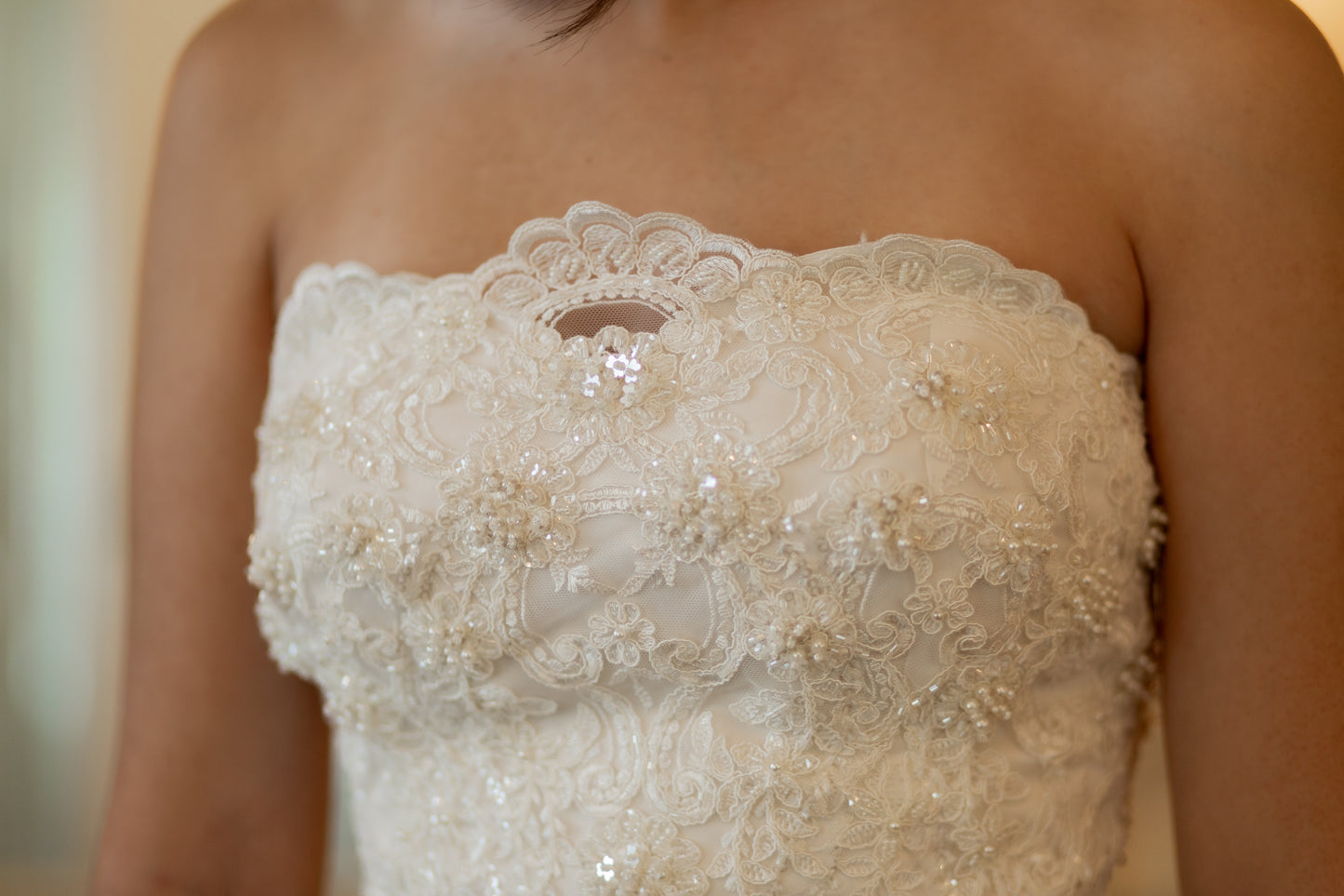 Close-up of 3D floral lace with pearls and sequins on the scalloped neckline edge.
