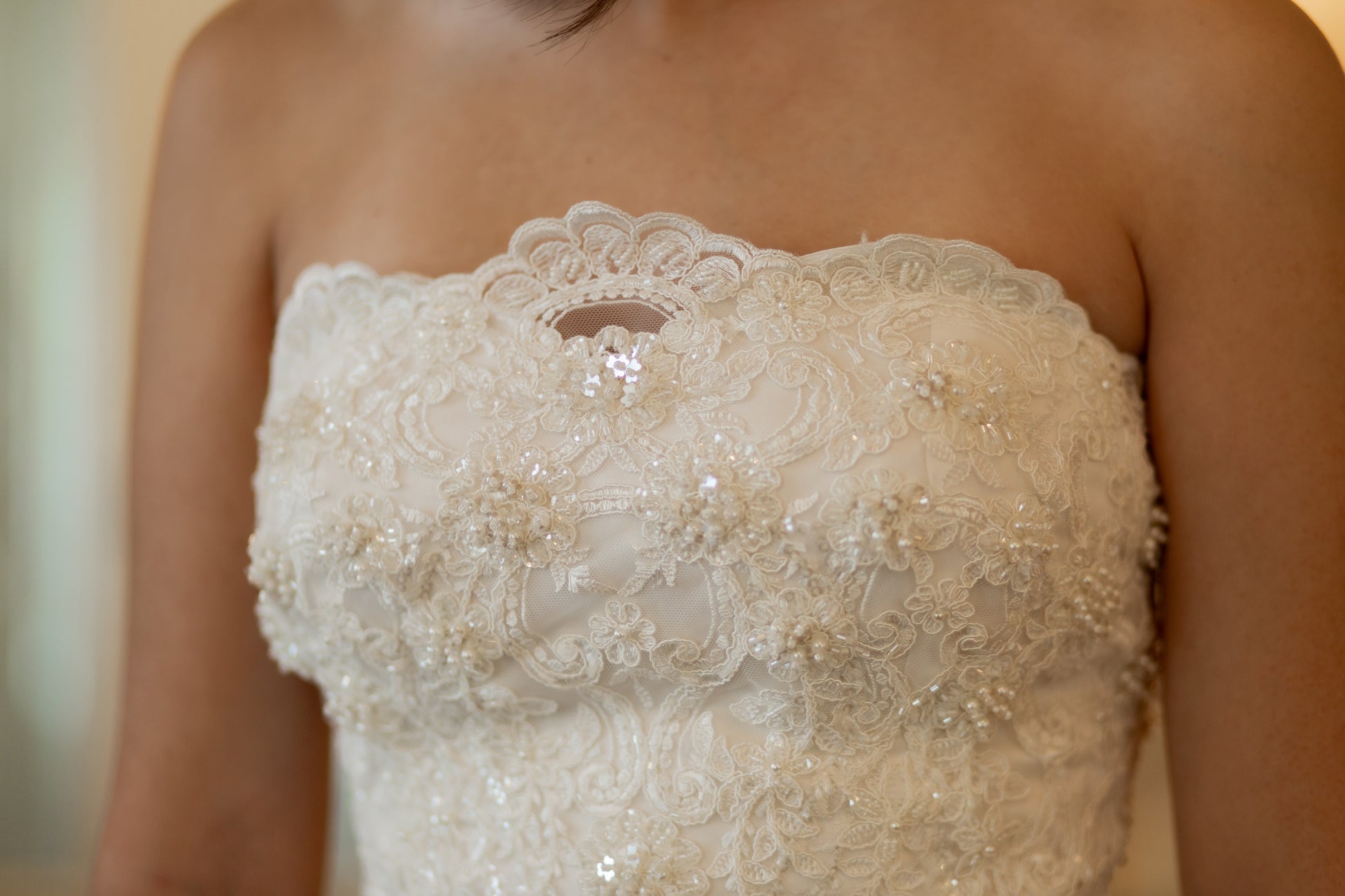 Close-up of 3D floral lace with pearls and sequins on the scalloped neckline edge.
