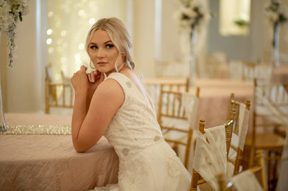 A bride wears the Poppy gown and sits at a table leaning forward. You can see the structured lace bodice and the way the lace trails down into the tulle skirt. 