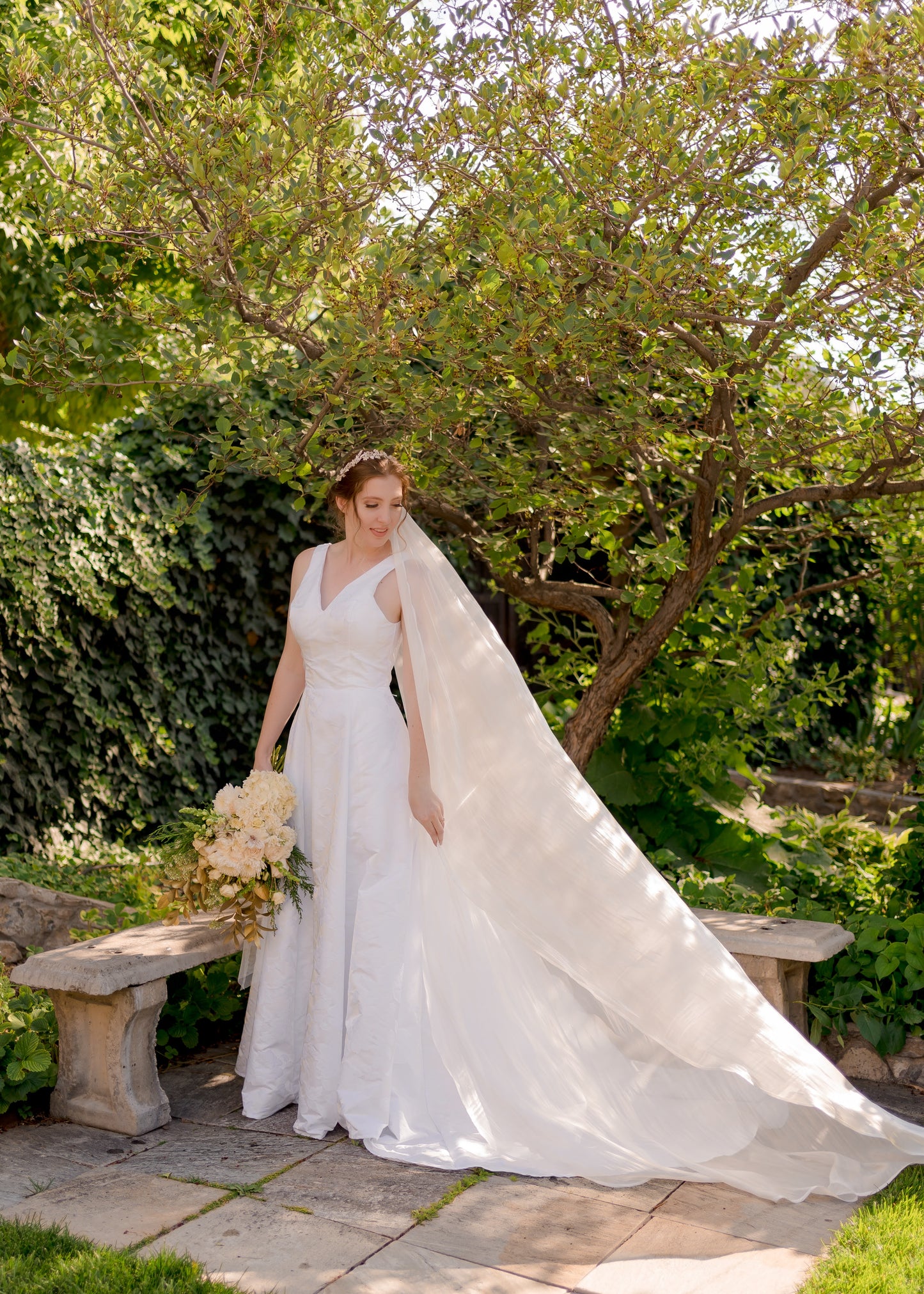 A bride wearing the flowing organza bridal veil, cara, with fluid movement and a clean edge as it flows behind the bride. It is styled here with our Madison gown. 