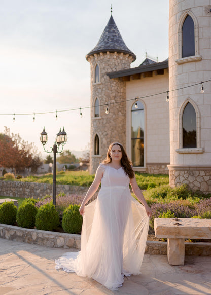 Bride wearing a Pale ivory wrap-style tulle overskirt, deon, with train shown over fit-and-flare gown, alora.