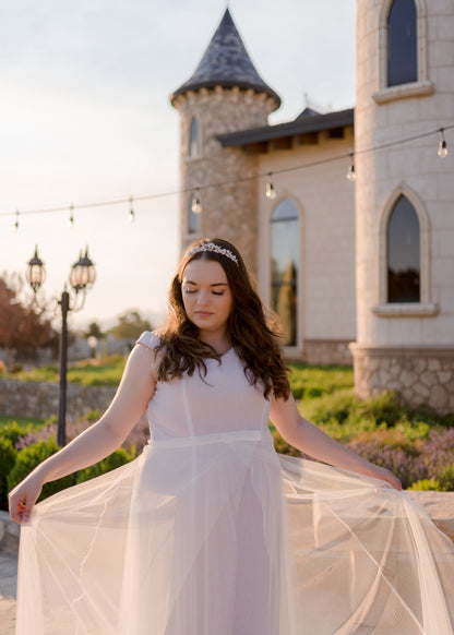 a bride wears the den soft tulle removable bridal skirt over her ft and flare gown; she is holding the sides of the skirt out showing off the layers. 