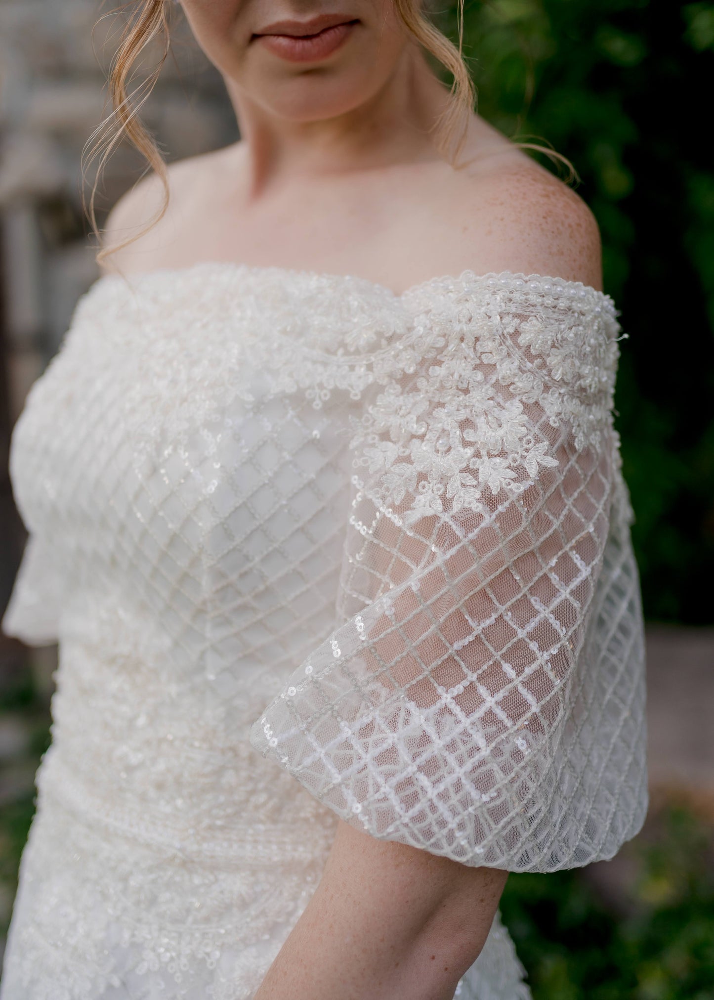 Wedding dress, parker, on a model. Close up detail shot of the puff sleeve, structured bodice, and off the shoulder lace detail. 