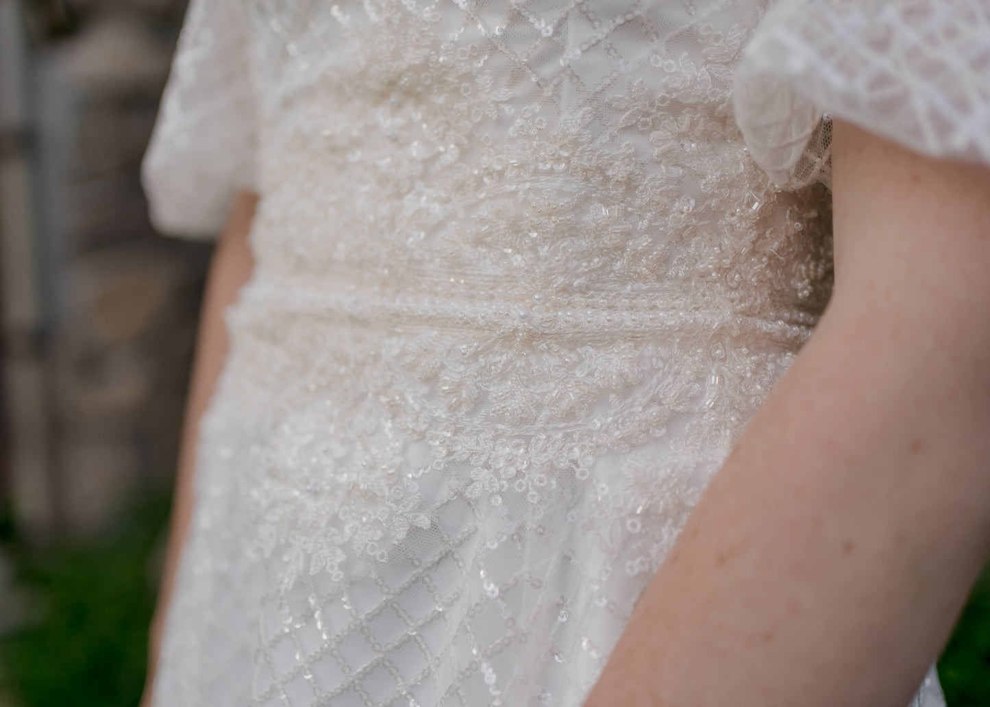 Close up detail of the waist with the beaded lace trim stretching up the bodice and down the skirt. The same trim detail follows the hem and off the shoulder neckline.  