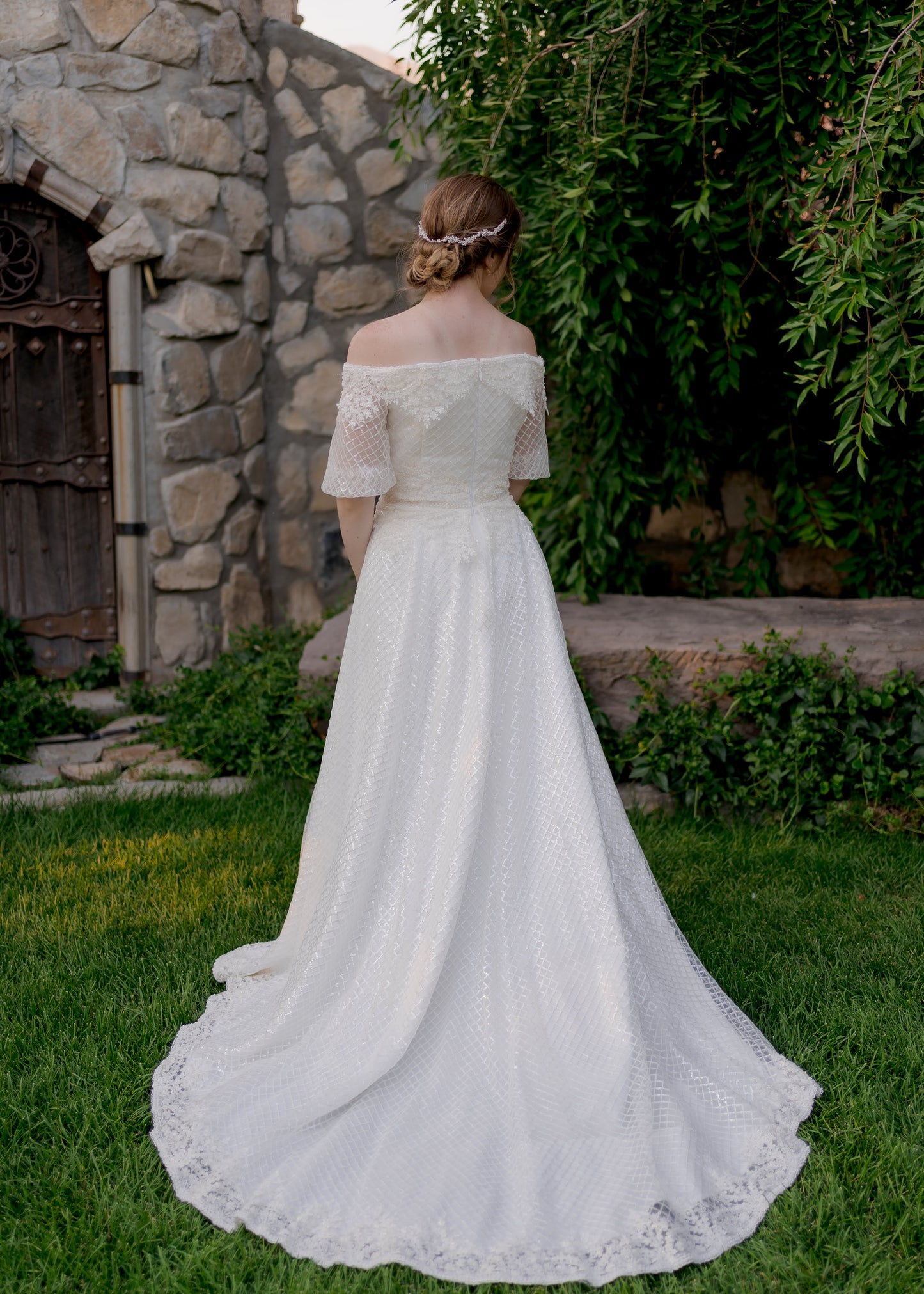 A full length back shot of the Parker wedding gown with the medium length train, sequined tulle overlay and off the shoulder puff sleeves. 