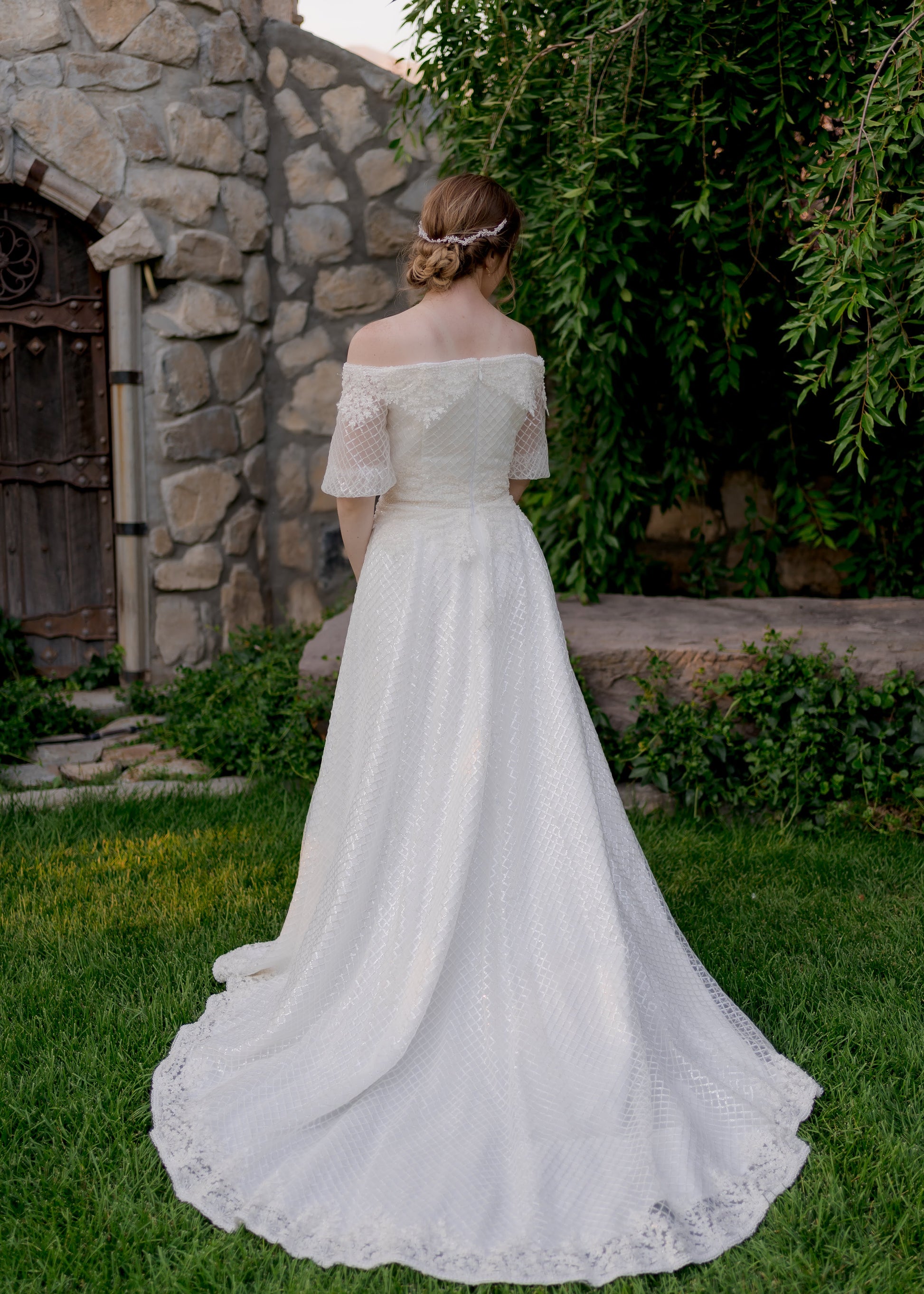 A full length back shot of the Parker wedding gown with the medium length train, sequined tulle overlay and off the shoulder puff sleeves. 
