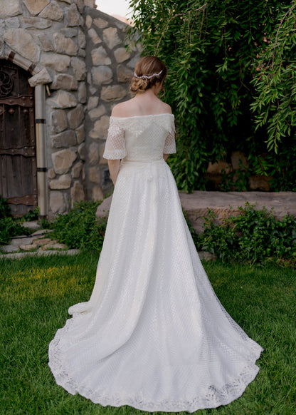 A full length back shot of the Parker wedding gown with the medium length train, sequined tulle overlay and off the shoulder puff sleeves. 