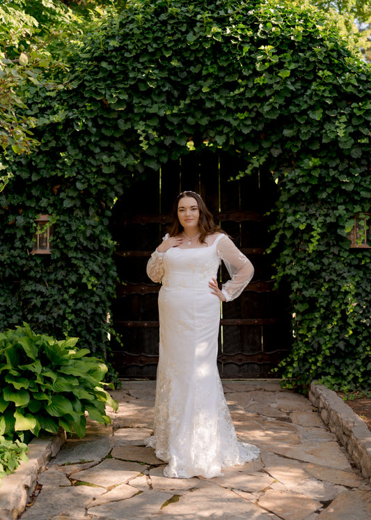 A full length image of the Violet wedding gown, showing off the gowns fit, sheer bishop sleeves, and square neckline. 
