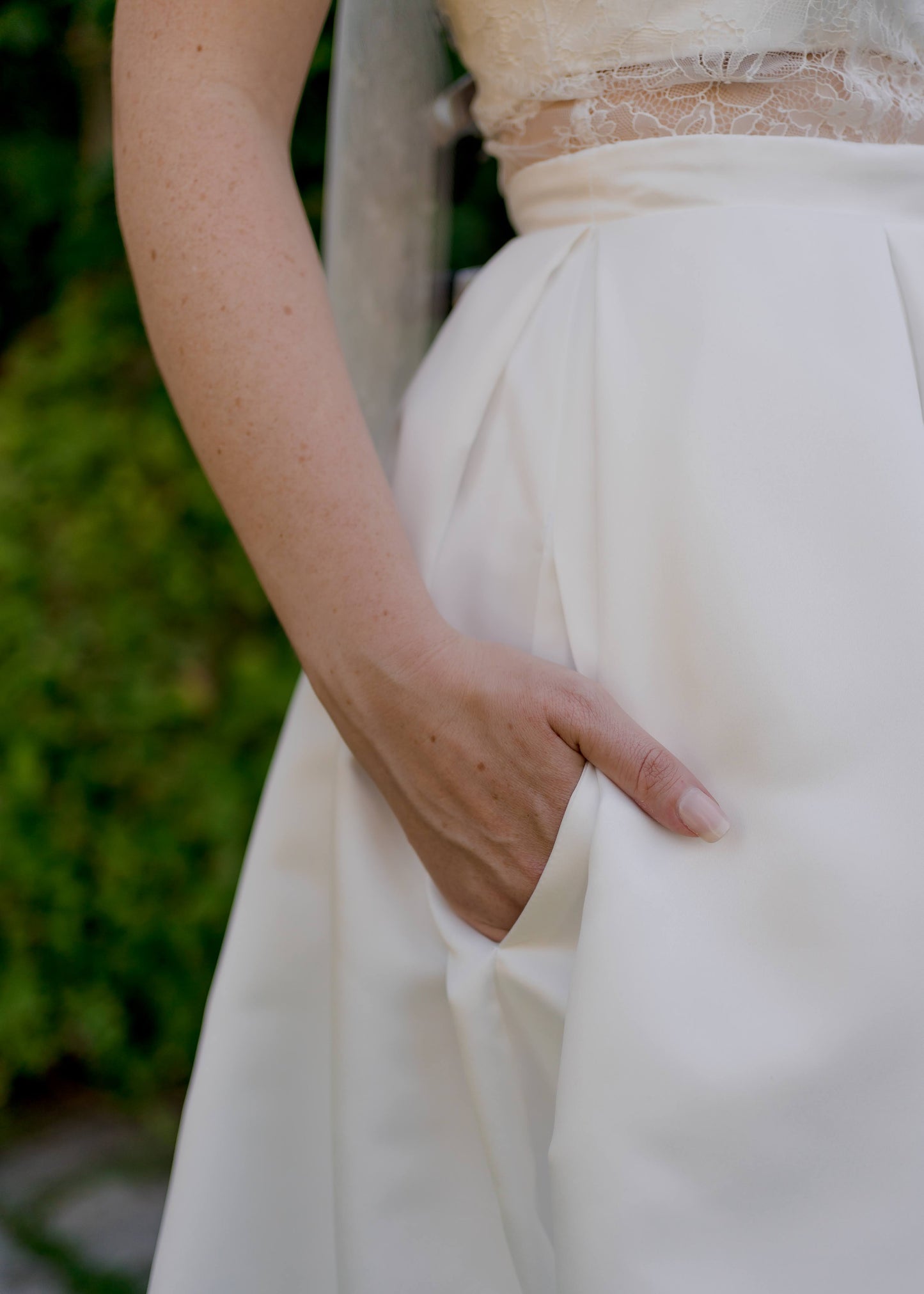 Close up of the Jessa gown; a bride has her hand inside the hidden inseam    pockets of the plain satin skirt. 