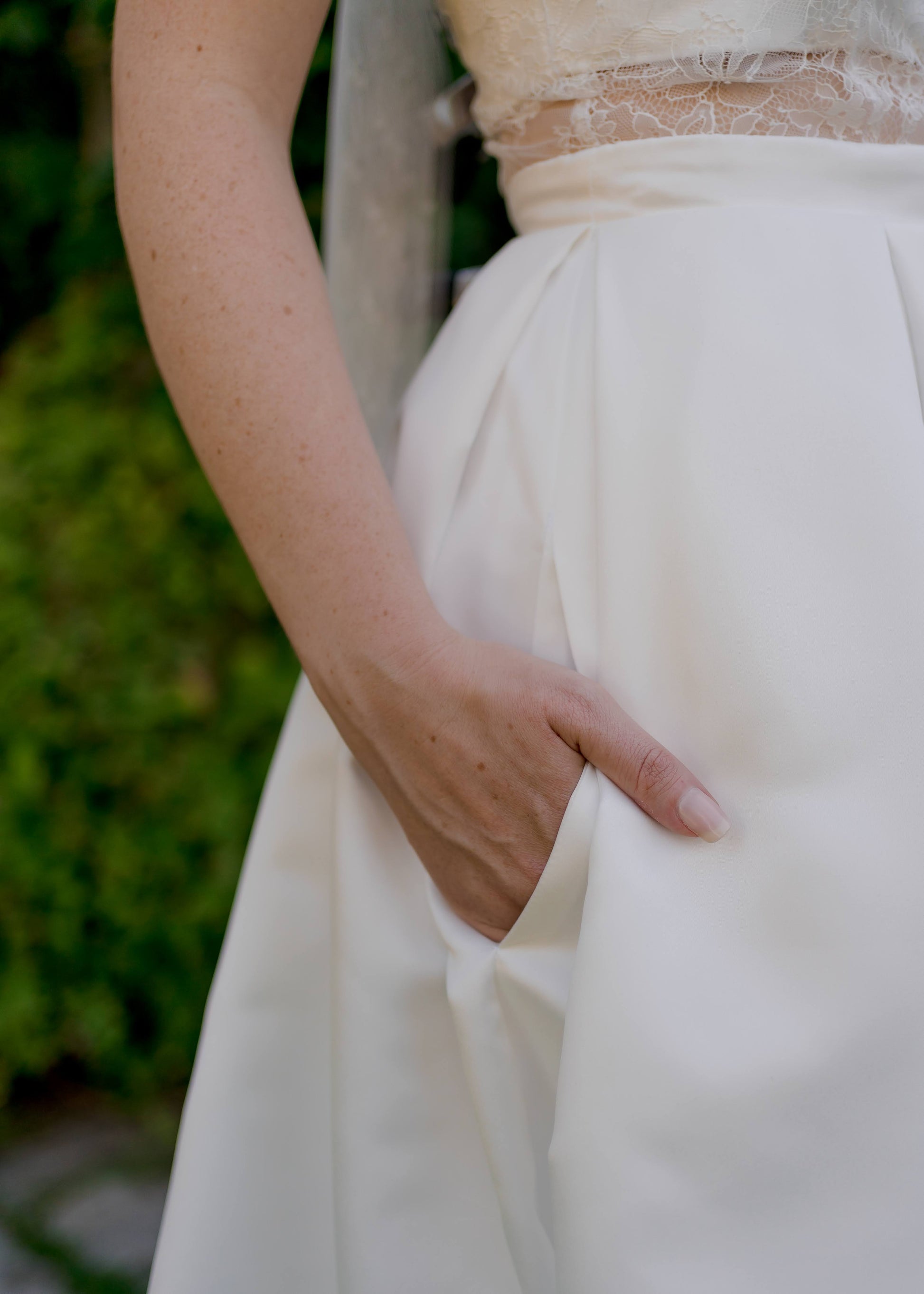 Close up of the Jessa gown; a bride has her hand inside the hidden inseam    pockets of the plain satin skirt. 