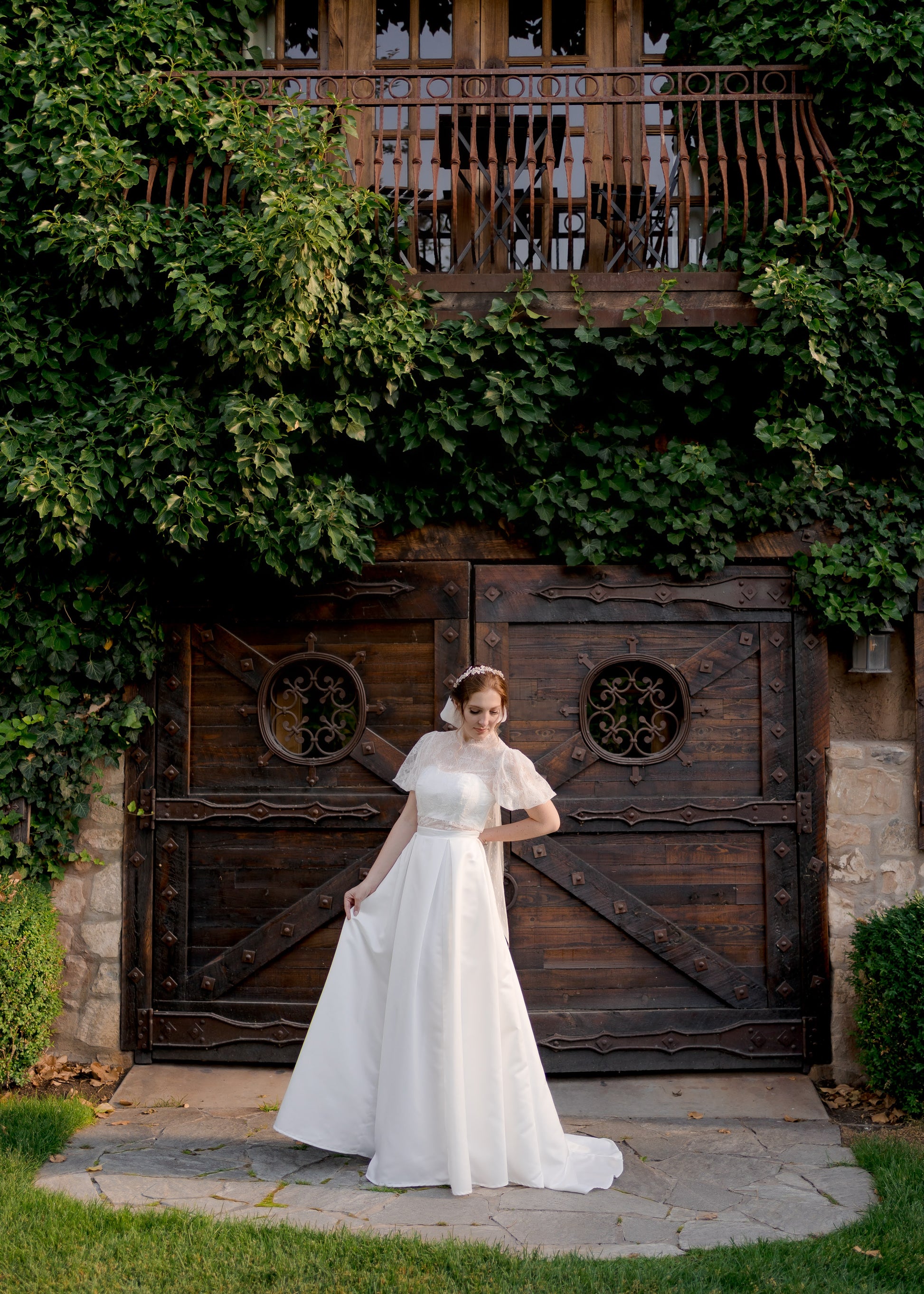 Jessa on a bride in a slightly turned stance showing the structured bando bodice with defined waistband and smooth pleated skirt. 