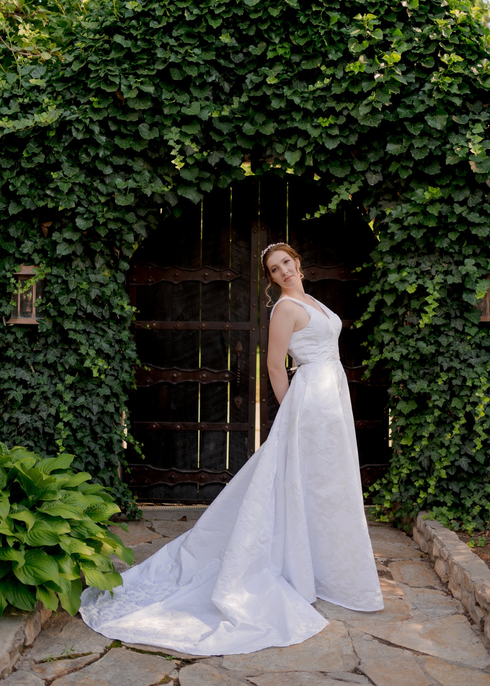 A styled shot of a bride in the madison gown; she stands sideways to the camera and leans back showing off the fitted bodice, the drape of the jacquard skirt and the 26-inch train flowing around the side.
