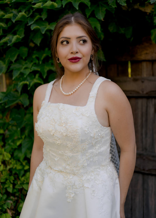 A close up front view of the Sabina gown with a square neckline, 1" wide straps, and 3d bridal lace that covers the bodice and extends down into the satin skirt. 