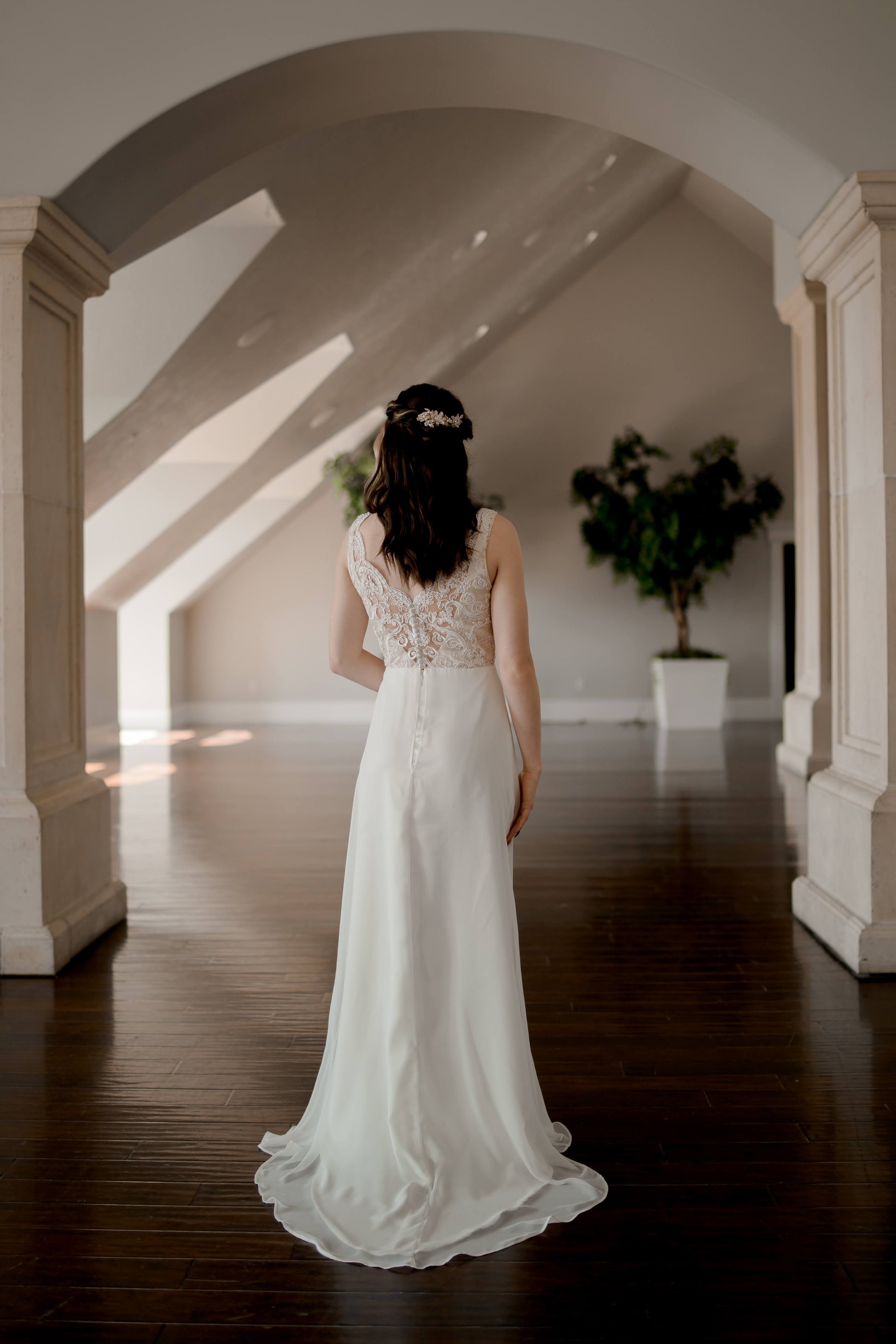 A full length back shot of the Winifred gown in Ivory on a bride with the flowy chiffon and satin train and the lace textured bodice. 