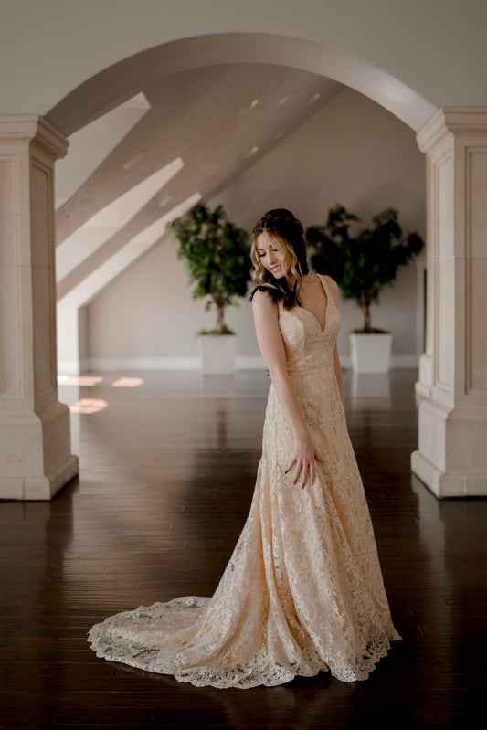 A side view of the trumpet margaret wedding gown on a bride with the salloped train flowing to the side as the bride looks back at it. 